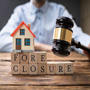 Judge’s gavel beside a small house and blocks spelling foreclosure on a table